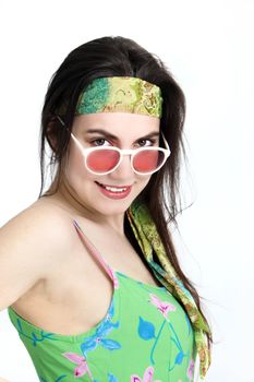 Sexy woman wearing a headband tilting her head and looking over the top of her rose coloured glasses with a smile isolated on white