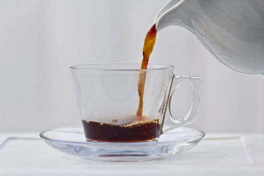 Pouring coffee into a quarter full clear cup with a saucer.