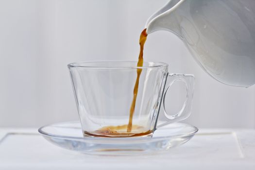 Pouring a small amount of coffee into a clear cup with a saucer.