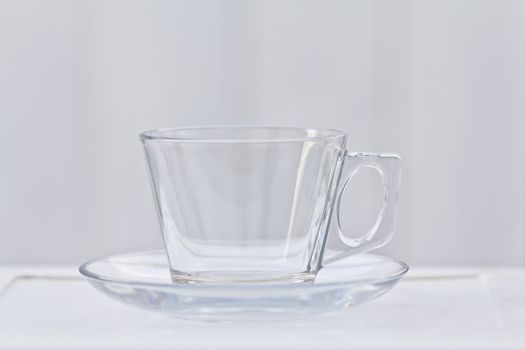 A clear glass coffee cup with a saucer that is empty.