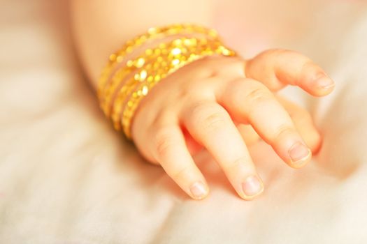 Baby hand with yellow gold bracelets, isolated towards white silk