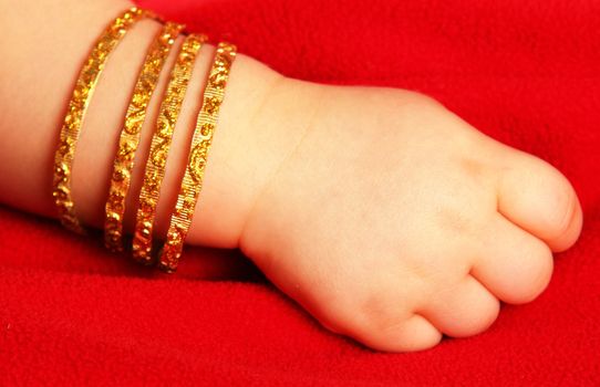 Baby hands, with a golden bracelet, isolated towards dark red
