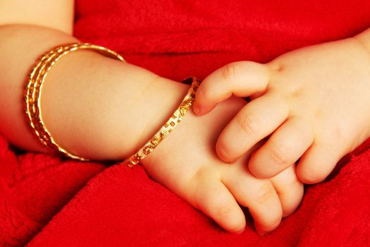 Baby hands with bracelets of yellow gold, isolated towards dark red