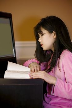 Ten year old biracial Asian girl sitting at computer desk, reading or studying