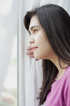 Side profile of teen girl or young woman looking out sunny window, happy or peaceful expression