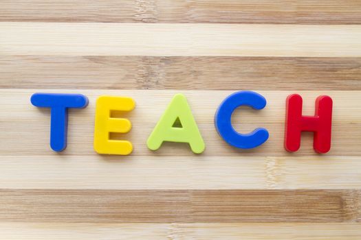 Letter magnets "TEACH" closeup on wood background 