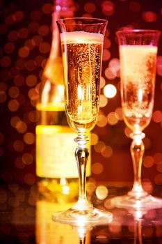 Champagne glasses and bottle over holiday bokeh background, focus on first glass 