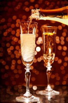 Champagne pouring into elegant glass over holiday bokeh background 