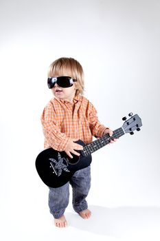 Funny little boy with ukulele guitar, studio shot 