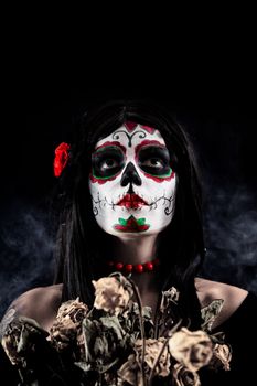 Sugar skull girl with dead roses, studio shot over black smoky background 