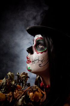 Sugar skull woman in tophat, holding dead roses, studio shot 