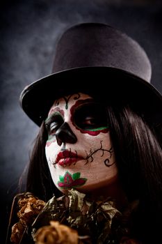 Sugar skull girl in tophat holding dead roses, studio shot 