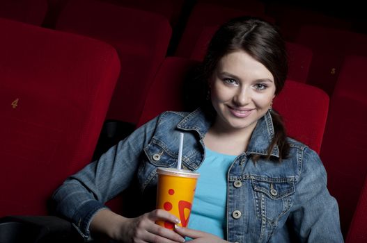 beautiful woman in a movie theater, watching a movie and drink a drink