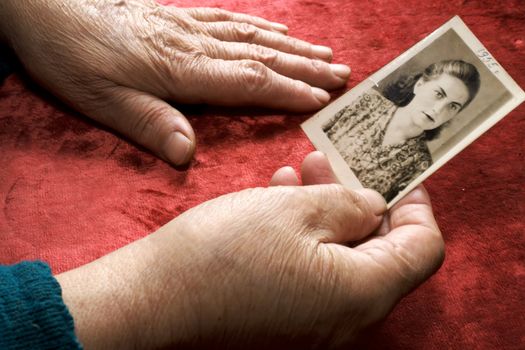 Old hands keep a photo of a young woman