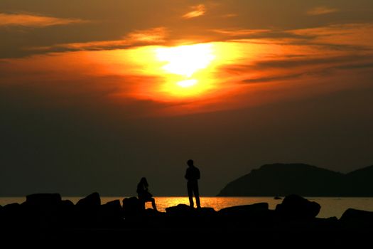 Sunset with people silhouettes on a rock beach at Thassos island, Greece