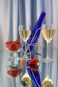 Two glasses of white wine with dark blue bottle and strawberries