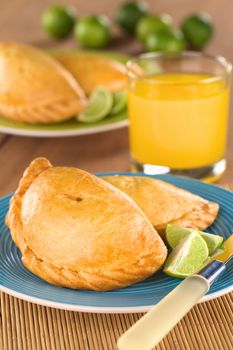 Peruvian snack called Empanada (pie) filled with chicken and beef served with limes (Selective Focus, Focus on the middle front part of the empanada)