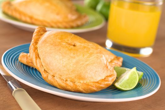 Peruvian snack called Empanada (pie) filled with chicken and beef served with limes (Selective Focus, Focus on the middle front part of the empanada)