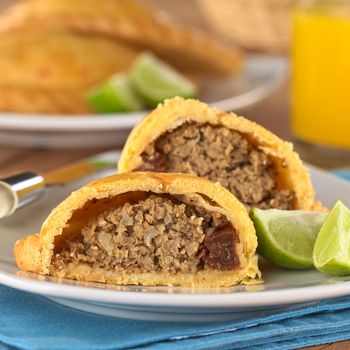 Peruvian snack called Empanada (pie) filled with beef and raisin served with limes (Selective Focus, Focus on the empanada stuffing in the front)