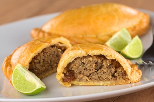 Peruvian snack called Empanada (pie) filled with beef and raisin served with limes (Selective Focus, Focus on the empanada stuffing in the front)