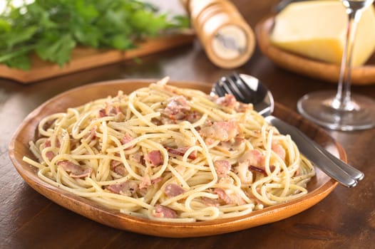 Spaghetti alla Carbonara served on wooden plate (Selective Focus, Focus one third into the meal)