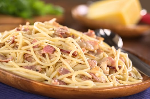 Spaghetti alla Carbonara served on wooden plate (Selective Focus, Focus one third into the meal)