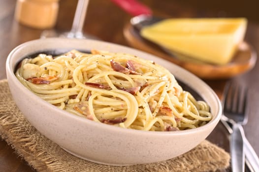 Spaghetti alla Carbonara made with bacon, eggs, cheese and black pepper served in bowl with cheese to grate in the back (Selective Focus, Focus one third into the meal)