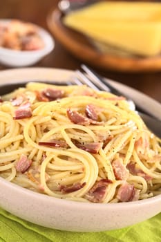 Spaghetti alla Carbonara made with bacon, eggs, cheese and black pepper served in bowl with cheese to grate in the back (Selective Focus, Focus one third into the meal)