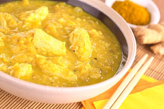 Chicken-mango curry with curry powder and ginger in the back (Selective Focus, Focus on the horizontal chicken piece in the middle of the bowl)