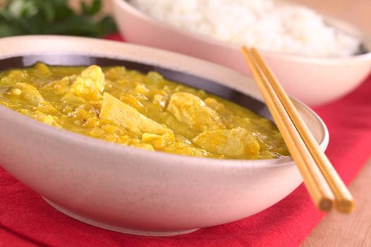 Chicken-mango curry with rice in the back (Selective Focus, Focus on the chicken pieces in the front)