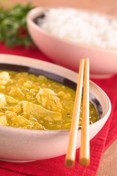 Chicken-mango curry with rice in the back (Selective Focus, Focus on the chicken one third into the bowl)