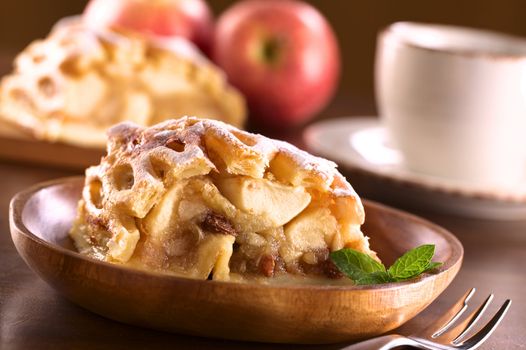 Apple strudel with raisins with coffee cup in back (Selective Focus, Focus on the left side of the apple-raisin stuffing and the front of the mint leaf)