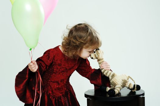 An image of a little girl in red dress with balloons and a toy