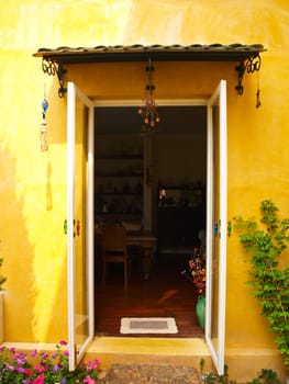 Yellow house wall with opened door and flower