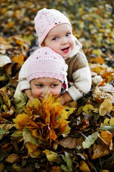 Two sisters playing with yellow leaves in a park