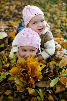 Two sisters playing with yellow leaves in autumn park