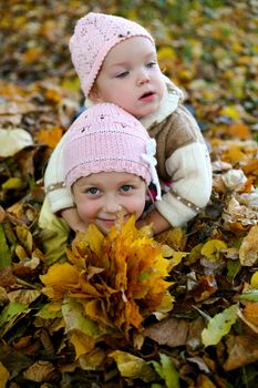 Two sisters playing with leaves in autumn park