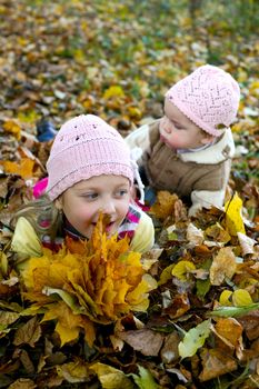 Two sisters playing with yellow leaves in autumn park