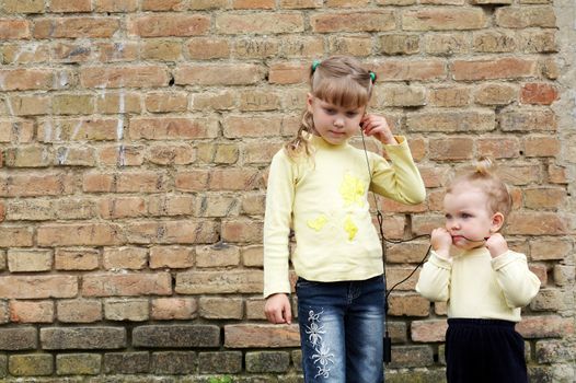 Two sisters listens to music on a background of a brick wall