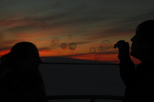 Silhouettes of the loving couple at sunset, blow bubbles