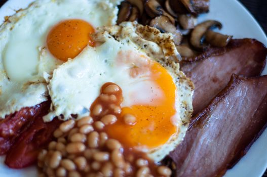 Traditional English breakfast - fried bacon, mushrooms, eggs, baked beens and tomatos