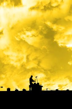 silhouette of a chimney sweep at work on the rooftop of a housing estate with sunset sky in background