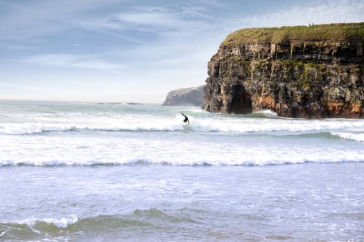 beautiful clean atlantic ocean with lone surfer catching the waves with cliffs in background on Irelands coast