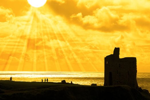 old castle in Ballybunion county Kerry Ireland at sunset with tourists and sun rays in background