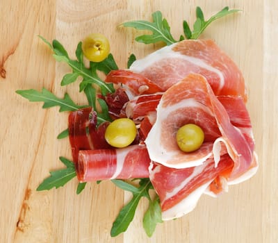 Slices of jamon and olives close up on wooden background