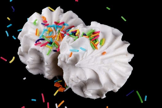 Two dessert marshmallows with coloured sugar grains isolated on black background