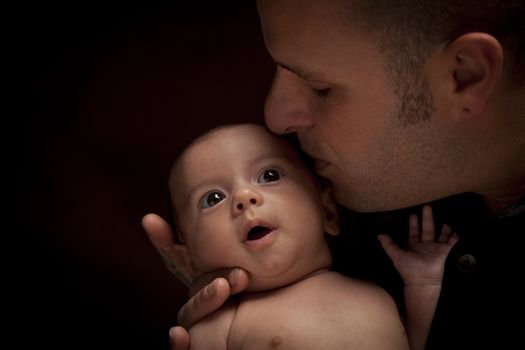 Happy Young Father Holding His Mixed Race Newborn Baby Under Dramatic Lighting.