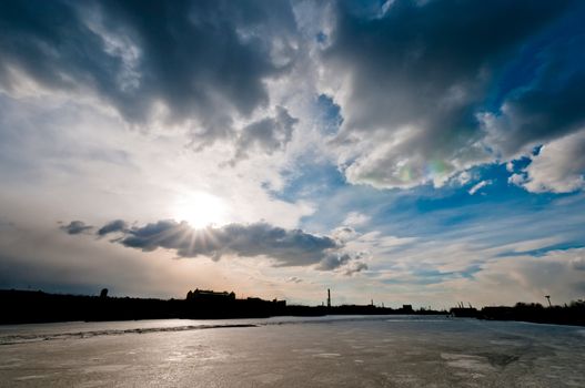 Cloudscape over the city silhouette and frozen river at winter