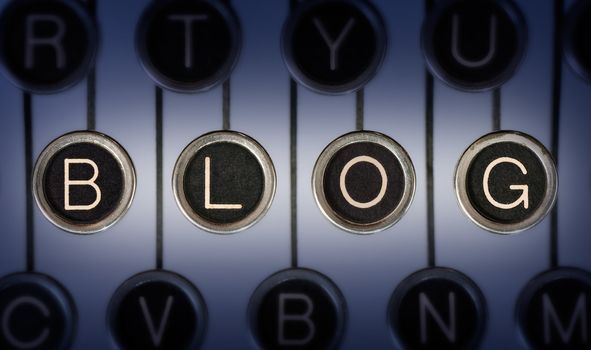 Close up of old typewriter keyboard with scratched chrome keys that spell out the word BLOG Lighting and focus are centered on BLOG 