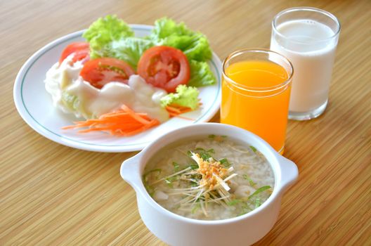 asian style rice soup with herbs in a bowl , fresh salad and milk , orange juice